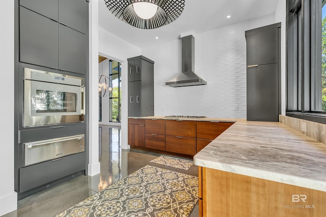 kitchen with wall chimney range hood, gray cabinetry, appliances with stainless steel finishes, and a wealth of natural light