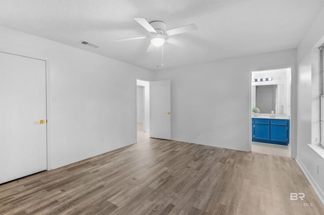 unfurnished bedroom featuring ensuite bathroom, ceiling fan, a textured ceiling, and light hardwood / wood-style flooring