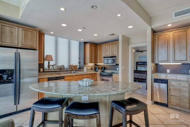 kitchen with appliances with stainless steel finishes, a kitchen island, a kitchen breakfast bar, and ceiling fan