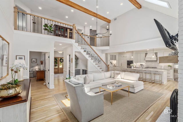 living room featuring beamed ceiling, light wood-style flooring, high vaulted ceiling, and stairs