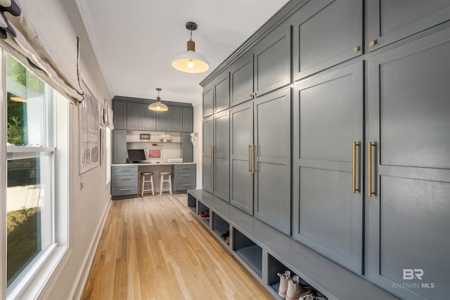 mudroom featuring built in desk, light wood-type flooring, baseboards, and ornamental molding