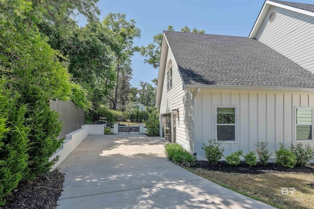 view of side of property with board and batten siding, roof with shingles, fence, and driveway