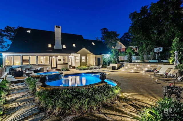 pool at night featuring fence, a patio area, a pool with connected hot tub, and an outdoor hangout area