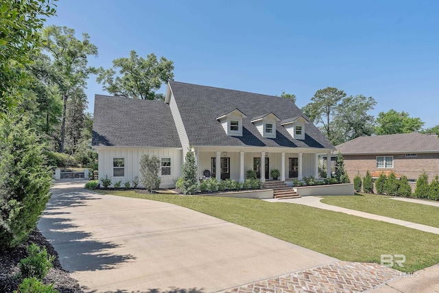 new england style home featuring concrete driveway, a front lawn, board and batten siding, covered porch, and roof with shingles