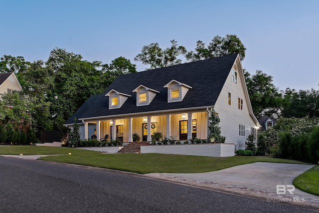 cape cod house with board and batten siding, roof with shingles, a front yard, and covered porch