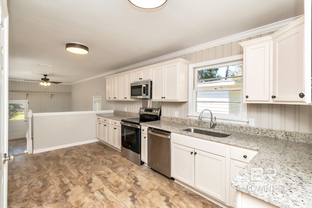 kitchen with white cabinets, appliances with stainless steel finishes, light stone counters, crown molding, and a sink