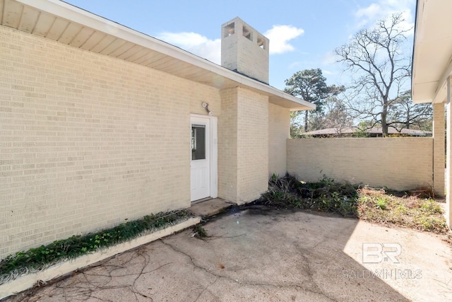 entrance to property with brick siding, fence, a chimney, and a patio