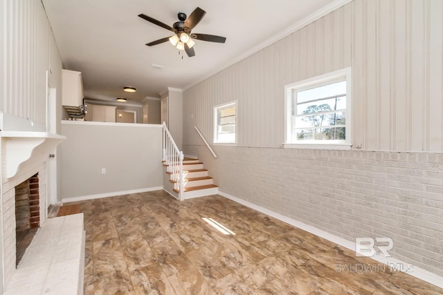 unfurnished living room featuring a ceiling fan, brick wall, stairway, ornamental molding, and a fireplace