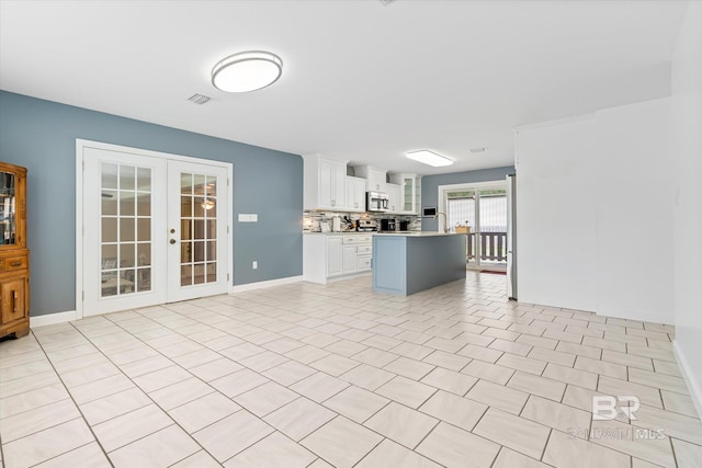 interior space featuring light tile patterned flooring, white cabinets, backsplash, a center island, and french doors