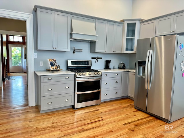 kitchen with appliances with stainless steel finishes, light wood-type flooring, gray cabinetry, and custom range hood