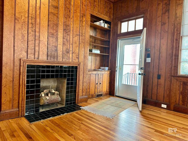 interior space with built in shelves, wooden walls, a fireplace, and hardwood / wood-style floors