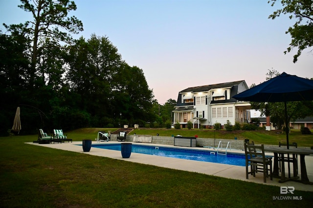 pool at dusk with a yard and a patio area