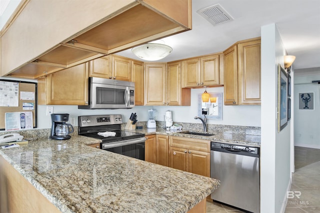 kitchen with visible vents, a peninsula, light stone countertops, stainless steel appliances, and a sink