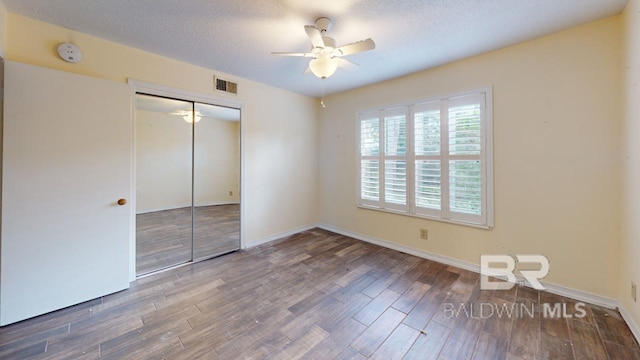 unfurnished bedroom featuring ceiling fan, dark hardwood / wood-style flooring, a textured ceiling, and a closet