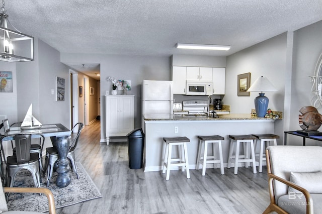 kitchen with white appliances, a peninsula, white cabinets, a kitchen bar, and light wood finished floors