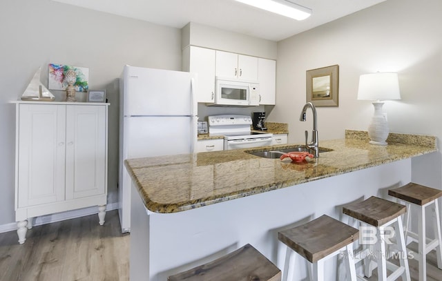 kitchen with white appliances, a peninsula, light wood-type flooring, a breakfast bar, and a sink