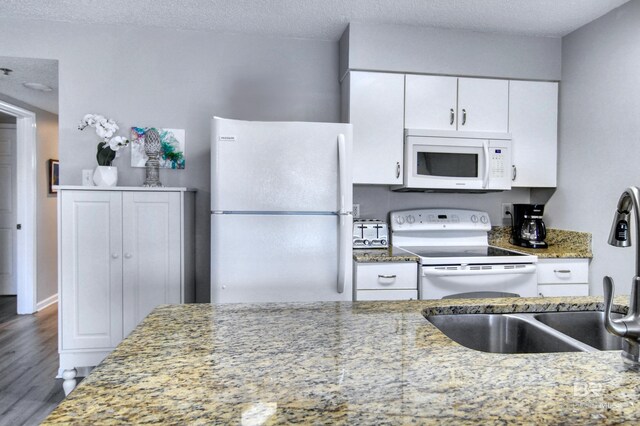 kitchen with white appliances, a textured ceiling, white cabinetry, wood finished floors, and light stone counters