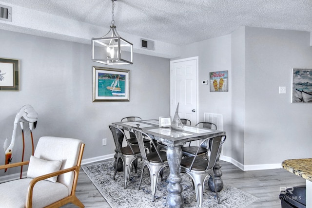 dining area featuring a textured ceiling, wood finished floors, baseboards, and visible vents