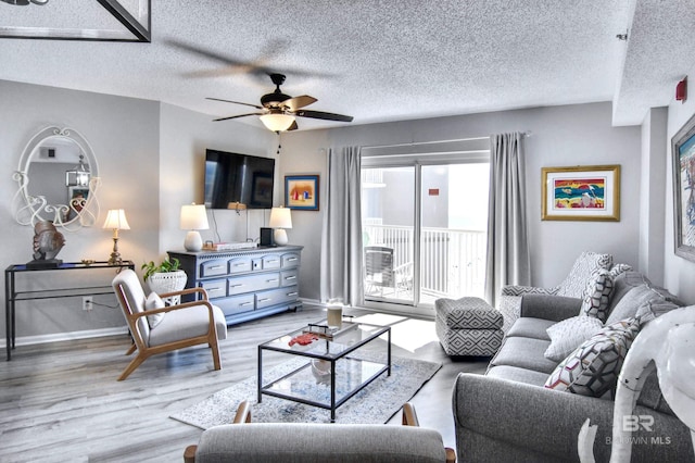 living room featuring baseboards, light wood-style flooring, a textured ceiling, and a ceiling fan