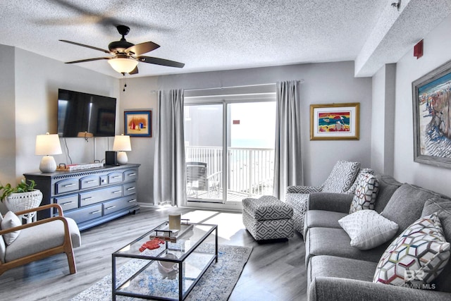 living room featuring a ceiling fan, light wood-style floors, and a textured ceiling