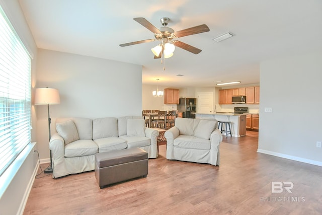 living room featuring baseboards, light wood finished floors, visible vents, and ceiling fan with notable chandelier