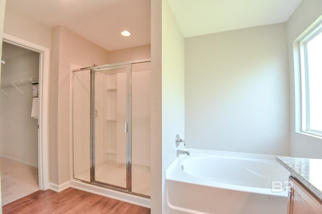 full bath featuring wood finished floors, vanity, a stall shower, a walk in closet, and a garden tub