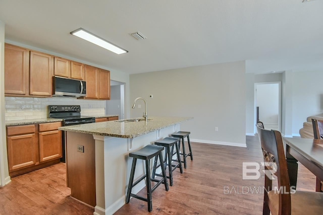 kitchen with black electric range oven, visible vents, a sink, stainless steel microwave, and light wood-style floors