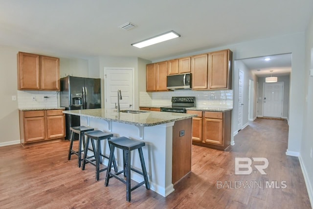 kitchen featuring a sink, wood finished floors, black appliances, visible vents, and decorative backsplash