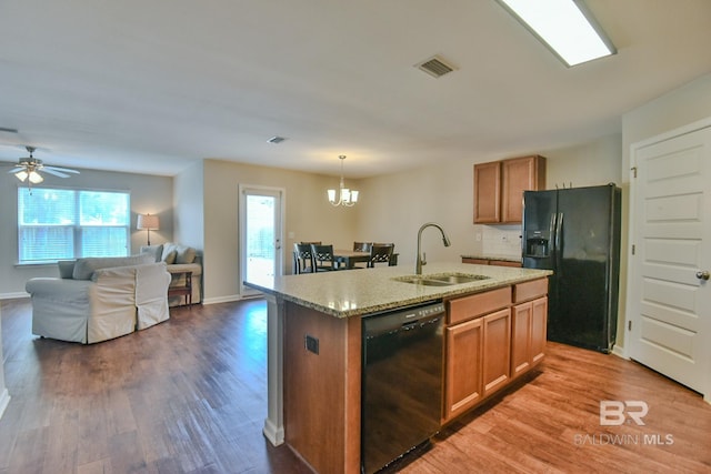 kitchen with a sink, brown cabinetry, wood finished floors, black appliances, and visible vents