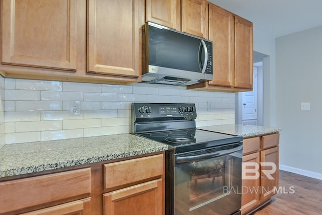 kitchen with light wood-style floors, light stone counters, black / electric stove, and stainless steel microwave