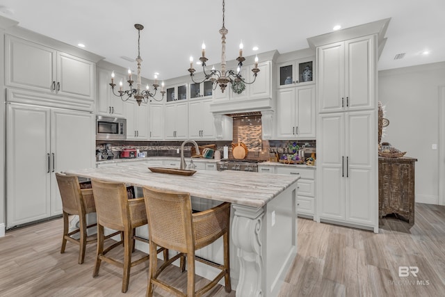 kitchen with pendant lighting, a kitchen island with sink, white cabinetry, built in appliances, and light stone counters