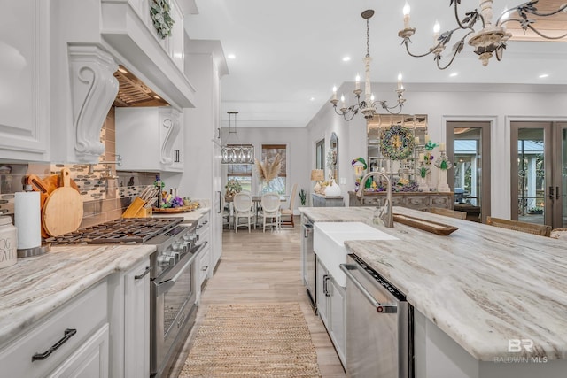 kitchen with stainless steel appliances, custom range hood, white cabinets, and decorative light fixtures