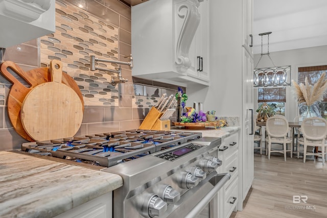 kitchen with stainless steel gas stove, white cabinetry, an inviting chandelier, light stone counters, and backsplash