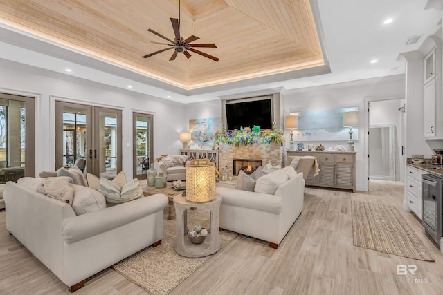 living room featuring french doors, a large fireplace, wine cooler, a tray ceiling, and light hardwood / wood-style flooring