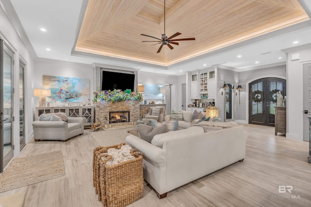 living room featuring a fireplace, french doors, wood ceiling, a tray ceiling, and light hardwood / wood-style flooring