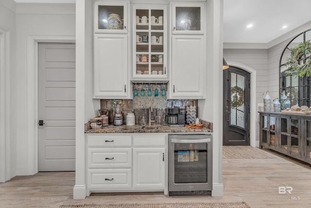 bar with dark stone countertops, backsplash, beverage cooler, and white cabinets