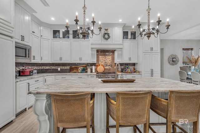 kitchen featuring light stone counters, built in appliances, an island with sink, and white cabinets