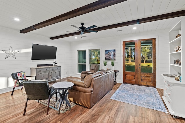 living room with french doors, light wood-type flooring, ceiling fan, wooden walls, and beamed ceiling