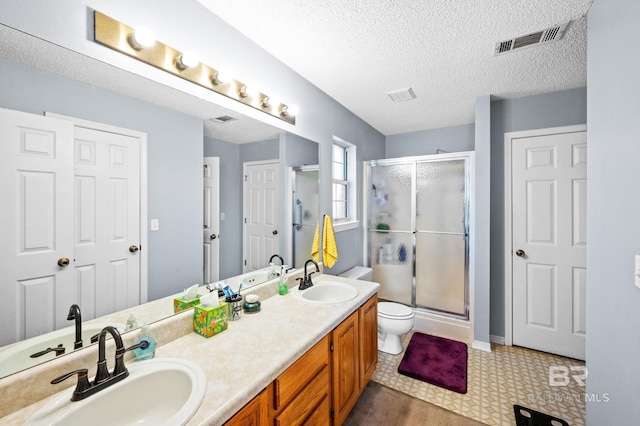 bathroom with a textured ceiling, vanity, toilet, and a shower with shower door