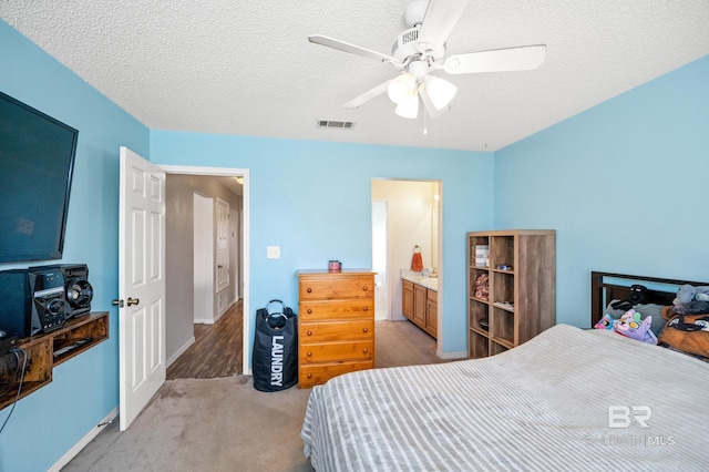 bedroom with ceiling fan, light colored carpet, a textured ceiling, and connected bathroom