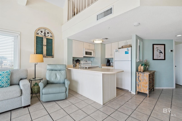 kitchen with a peninsula, open floor plan, visible vents, white appliances, and light countertops