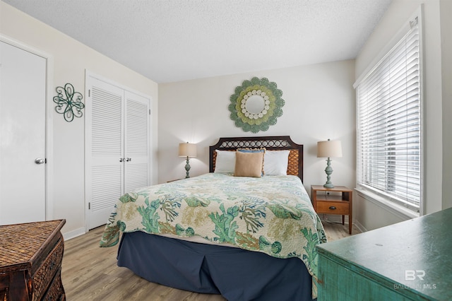 bedroom featuring a closet, a textured ceiling, wood finished floors, and baseboards