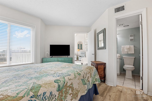 bedroom with a textured ceiling, baseboards, visible vents, and wood finished floors