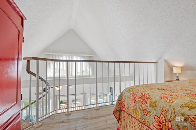 bedroom featuring lofted ceiling, multiple windows, a textured ceiling, and wood finished floors
