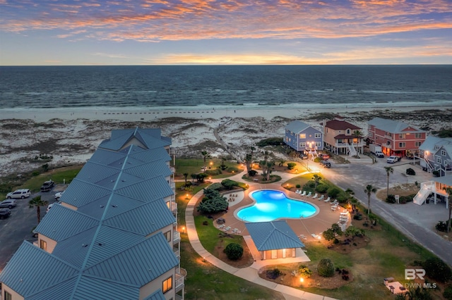 aerial view at dusk featuring a water view and a view of the beach
