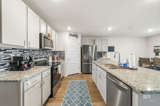 kitchen with a sink, decorative backsplash, appliances with stainless steel finishes, and an island with sink