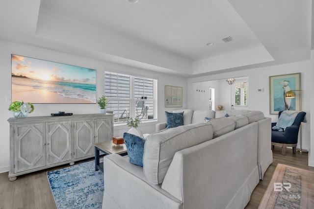 living room with visible vents, baseboards, a notable chandelier, light wood-style floors, and a tray ceiling