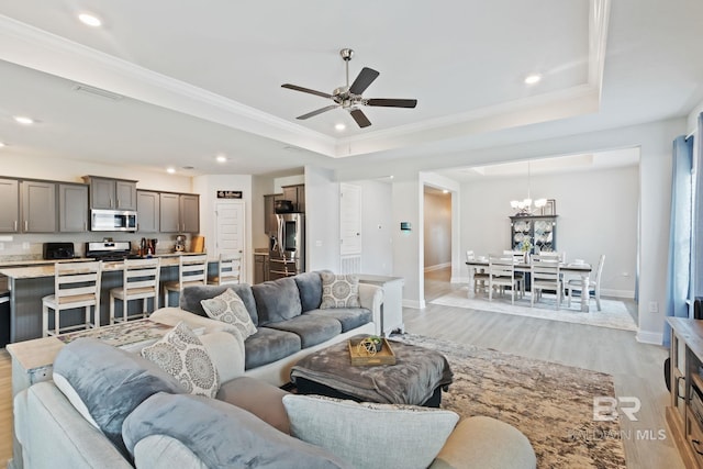 living room featuring ceiling fan with notable chandelier, light hardwood / wood-style floors, a raised ceiling, and crown molding