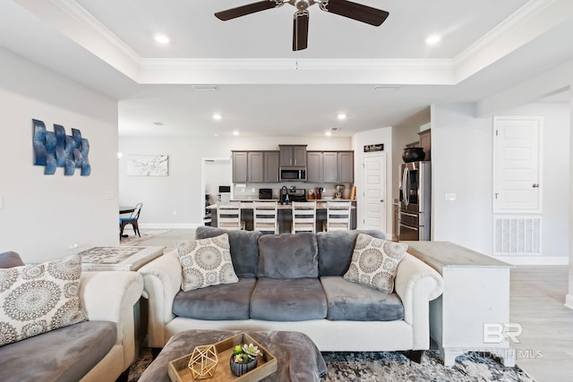 living room featuring a tray ceiling, light hardwood / wood-style floors, crown molding, and ceiling fan