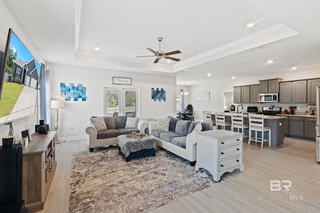 living room with ceiling fan, a tray ceiling, sink, french doors, and light hardwood / wood-style floors